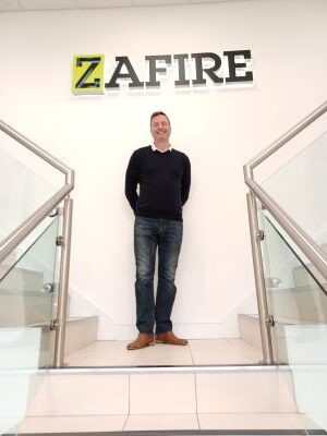 A photo of Zafire's new Head of Commercial, Grant Winter, standing beneath the company logo in the lobby at Zafire HQ in Banbury, UK.